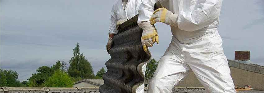 Two people in white safety suits and gloves carrying asbestos contaminated building material